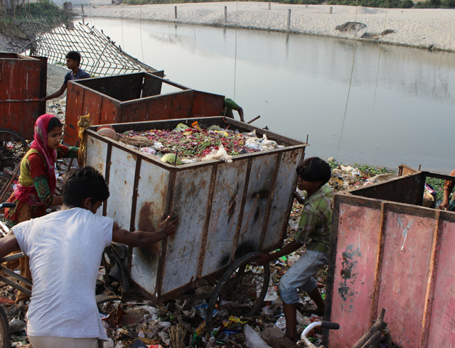 Workers dump trash from a rickshaw for use as landfill.